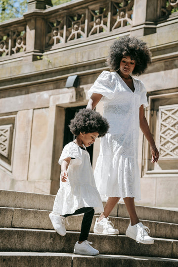 A mother folds gently used baby clothes at a kitchen table with natural light, surrounded by cardboard boxes ready for donation or swap, highlighting sustainable parenting choices.
