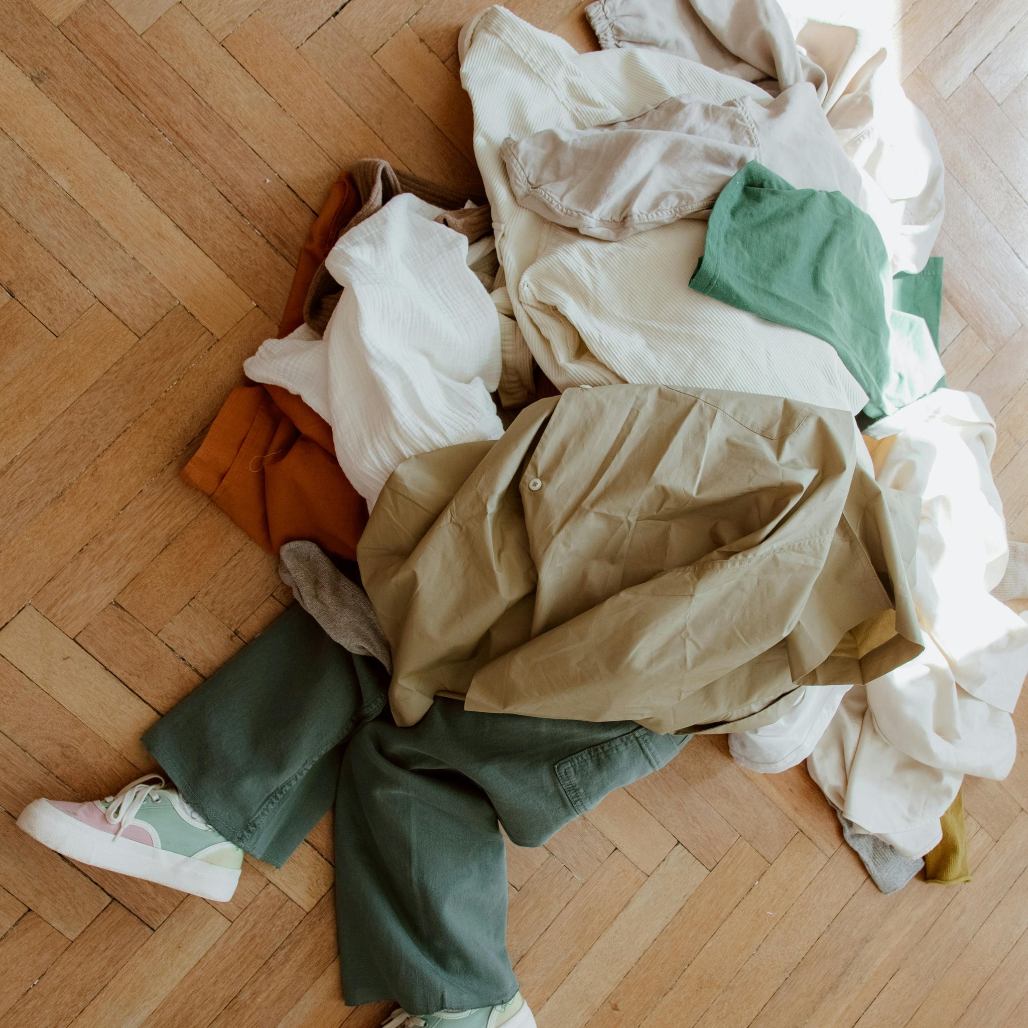 A mom and twoA child sits under a pile of gently used kids' clothes on the living room floor, that are ready donation or swapping.