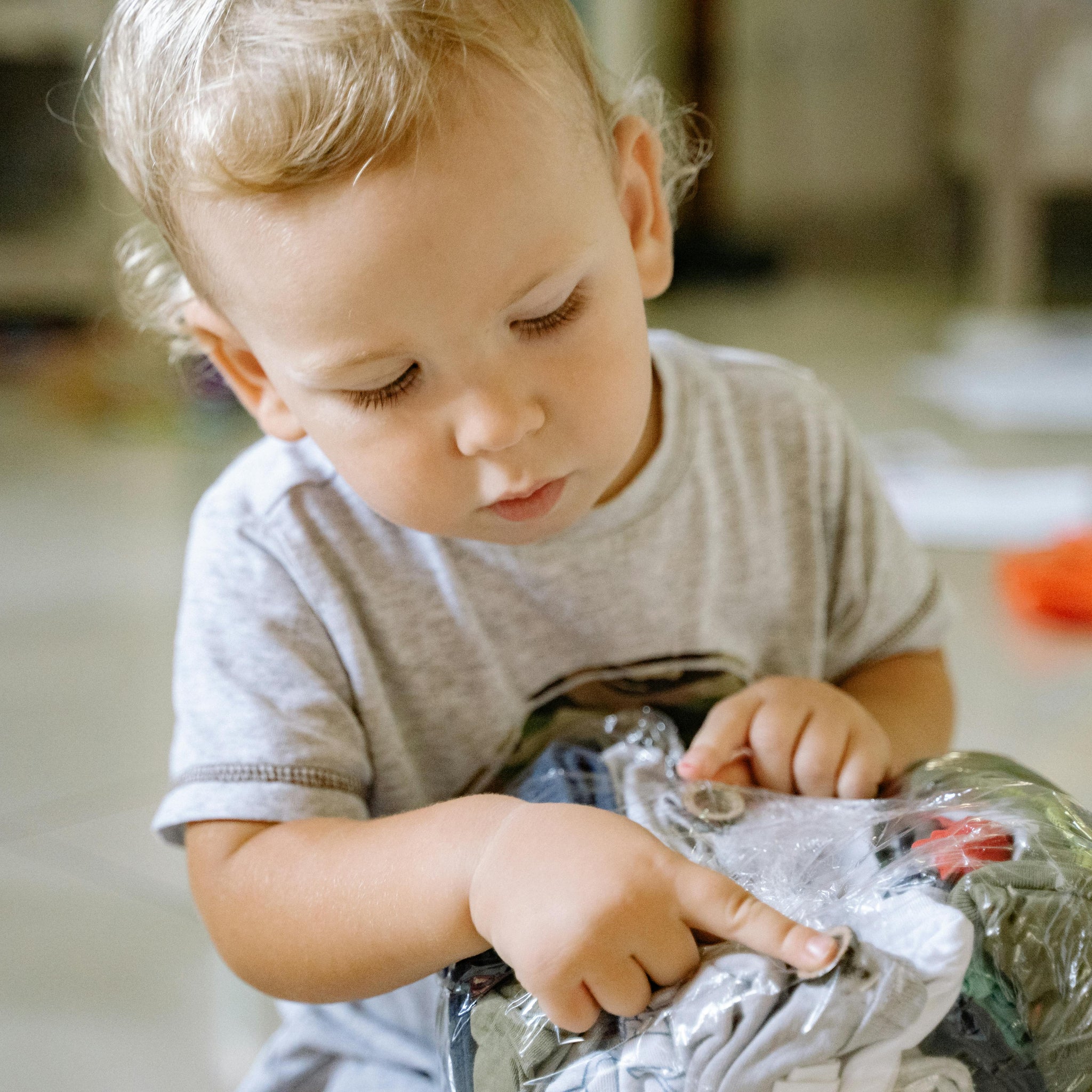 A young boy sits on the floor inspectingused kids clothes