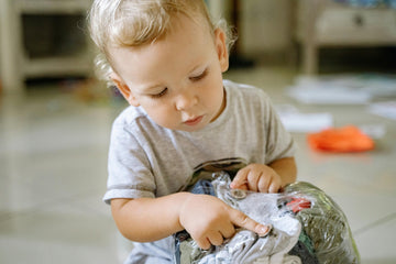 A young boy sits on the floor inspectingused kids clothes